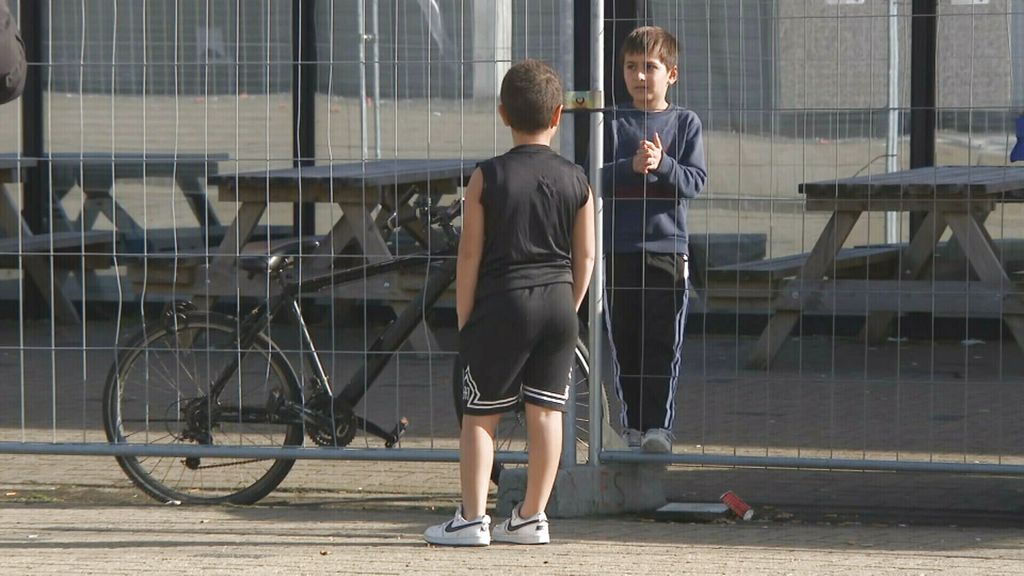 Kinderen praten bij een hek met fiets op achtergrond.