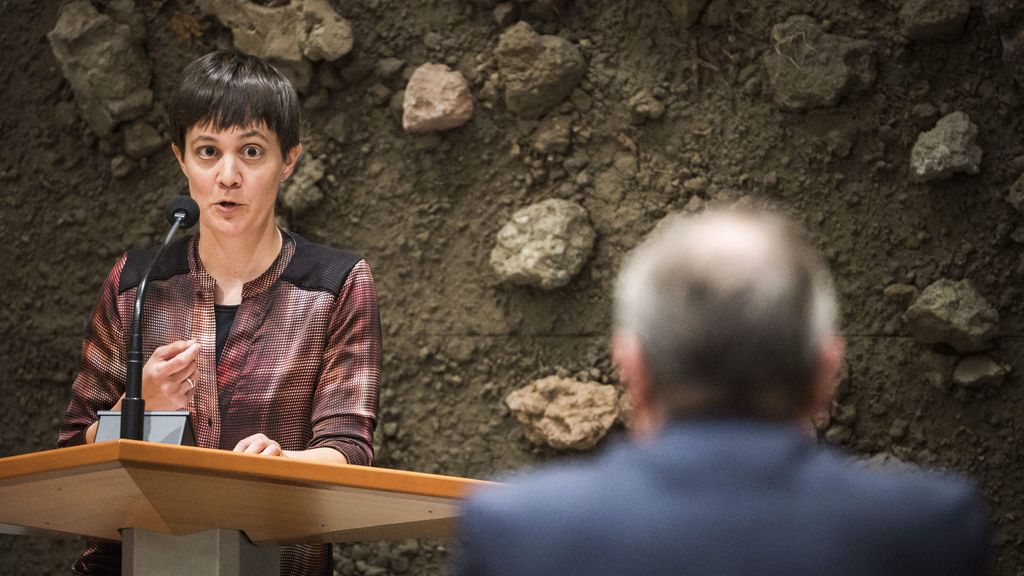 Vrouw spreekt op podium, man luistert in publiek.