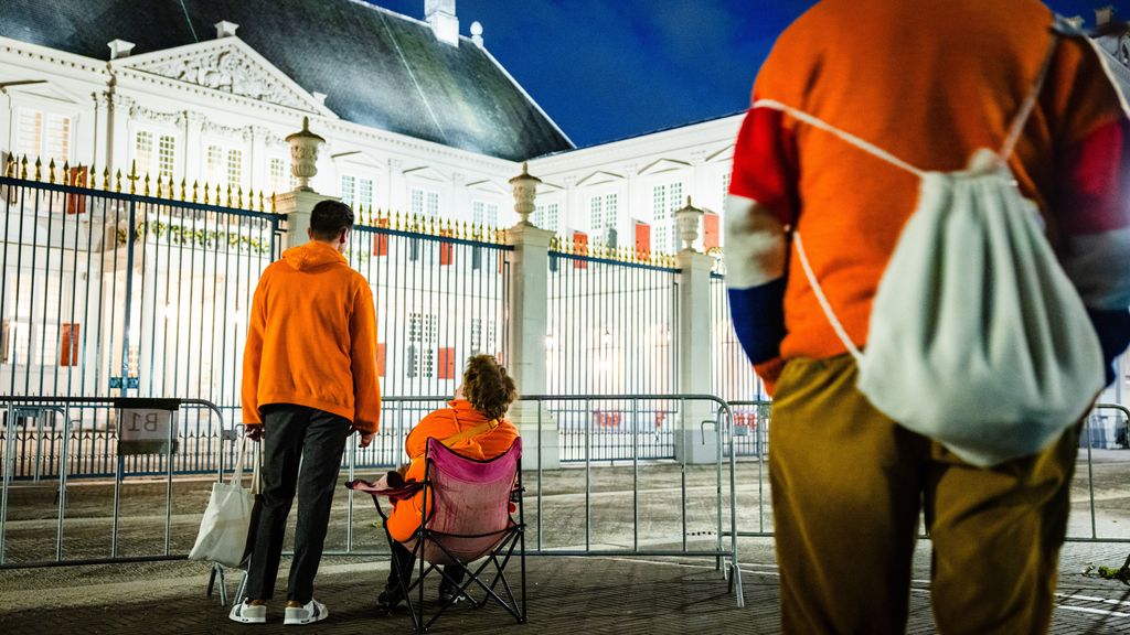 Mensen wachten bij paleishek in oranje kleding.