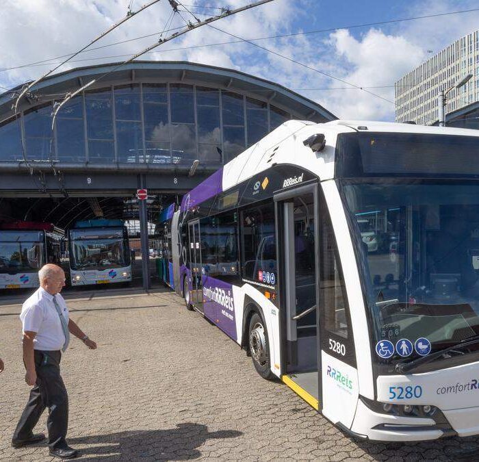 Mannen lopen voorbij busstation met elektrische bussen.