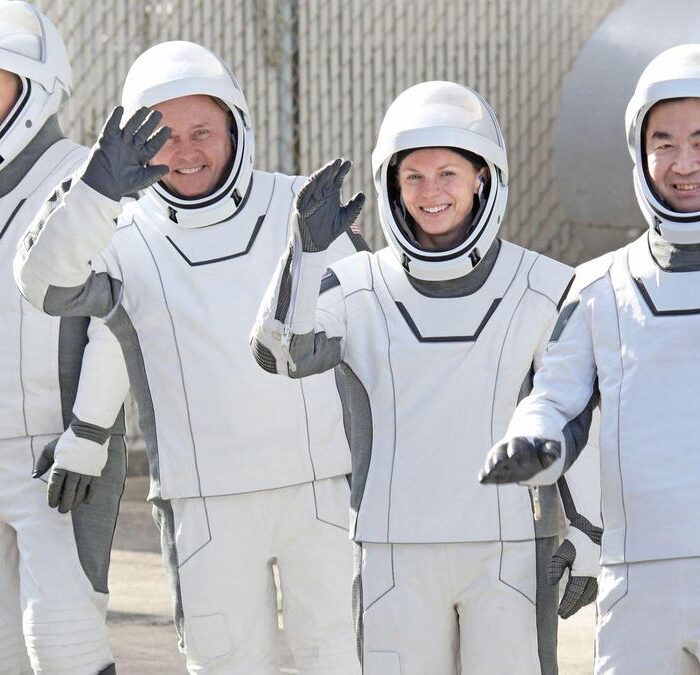 Astronauten in witte pakken zwaaien lachend.